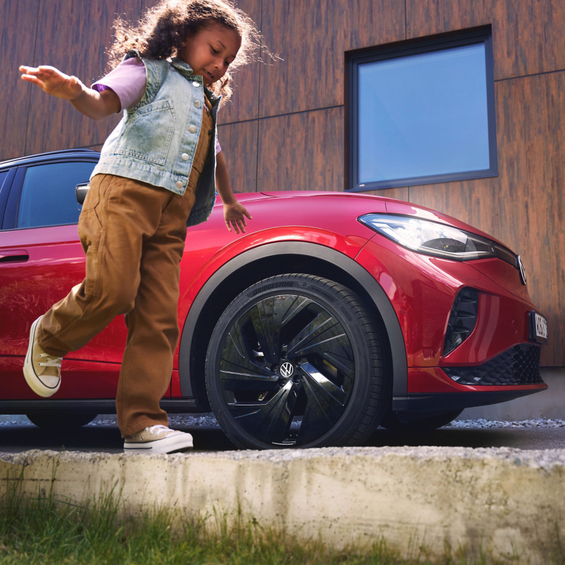 Ragazza che corre attorno a un VW ID.4 GTX parcheggiato davanti a una casa moderna.