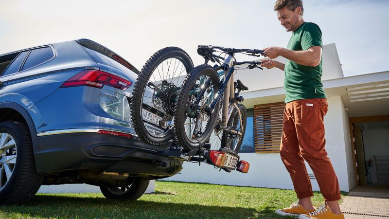 Man places two bicycles on VW Accessories bicycle carrier of VW Tiguan Allspace