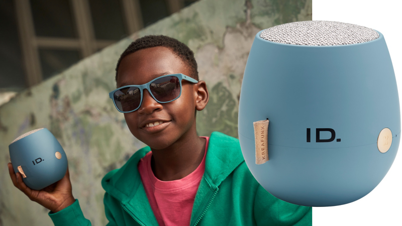 Kind mit Sonnenbrille hält einen Bluetooth®-Lautsprecher aus der ID. Kollektion von Volkswagen Zubehör in der Hand