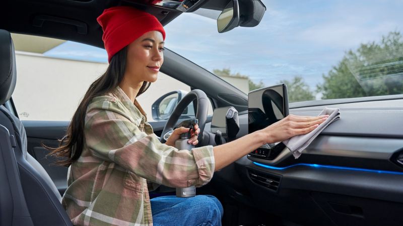 Frau reinigt die Armatur eines VW Autos mit Pflegemitteln von VW Zubehör