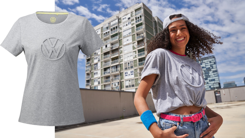 Frau trägt graues T-Shirt mit VW Logo in 3D aus der Volkswagen Kollektion, im Hintergrund Hochhäuser