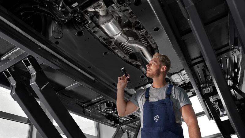 VW Servicemitarbeiter inspiziert den Unterboden eines VW Autos in der Werkstatt