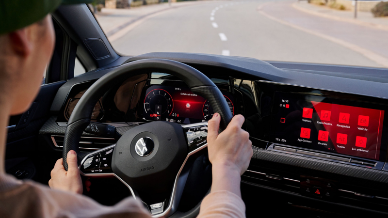 Woman at the steering wheel of a VW car, road is visible through the front windscreen