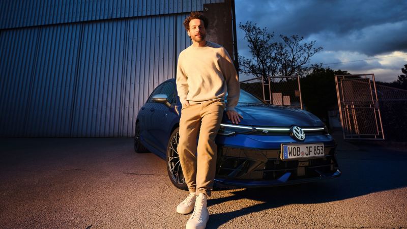 Man leaning against the front of a VW Golf R with illuminated LED crossbar