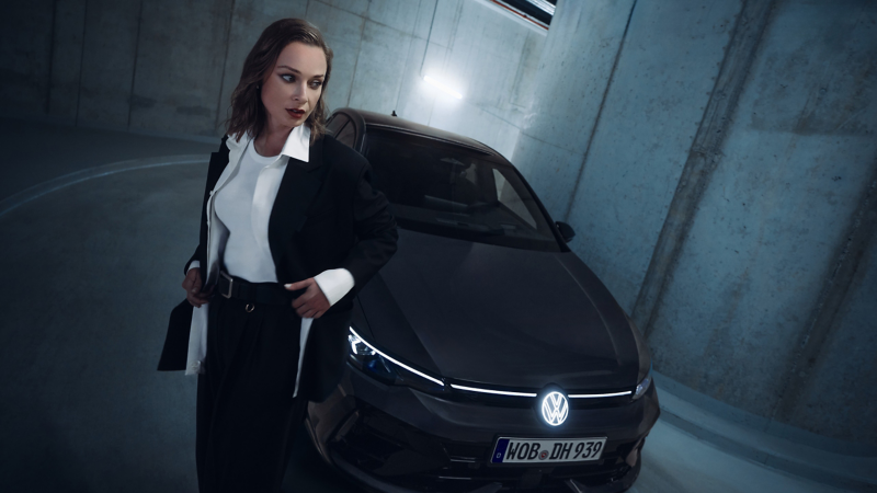 Un homme appuyé contre l’avant d’une VW Golf R, barre transversale LED allumée