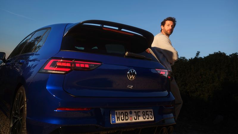 Mann lehnt an VW Golf R, Fokus auf Heckansicht