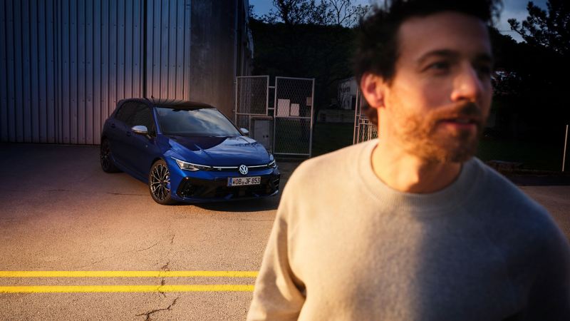 Fokus auf Mann, im Hintergrund VW Golf R vor einer Fabrikhalle