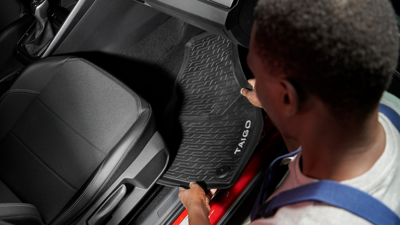 VW service employee places VW Accessories floor mat with “Taigo” writing in the footwell
