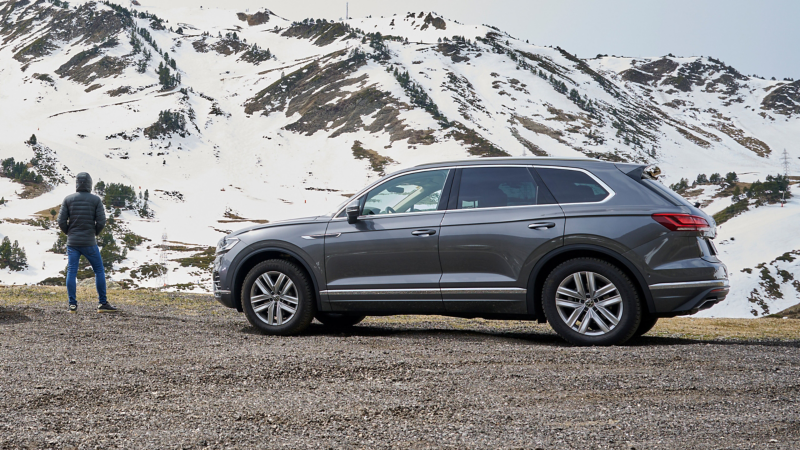 Person neben einem VW Auto vor verschneiter Berglandschaft