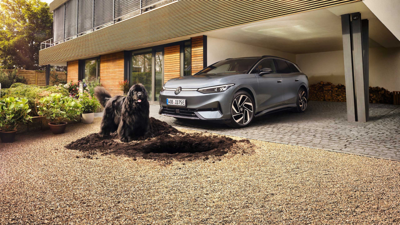VW ID.7 Tourer Pro unter Carport, davor ein schwarzer Hund, der Loch gebuddelt hat