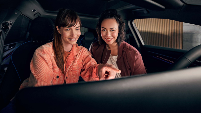 Zwei Frauen benutzen das Infotainment-System im VW Auto.