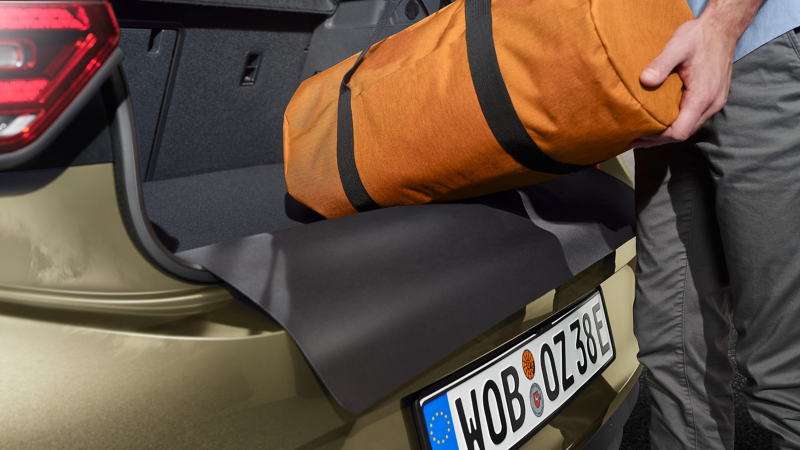 Une personne dépose un sac sur le tapis de coffre réversible des Accessoires VW dans le coffre d’une VW ID.3