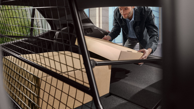 Un homme dépose des cartons dans le coffre, gros plan sur la grille de séparation de coffre issue des Accessoires VW