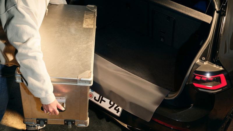 Mann belädt Kofferraum eines VW Golf R mit Kiste, VW Zubehör Gepäckraumwendematte dient zum Schutz