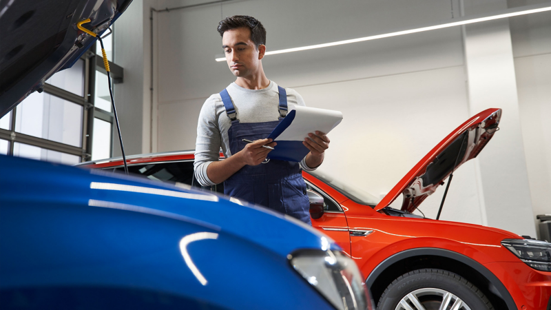 VWのサービススタッフがディーラーでボンネットを開けた2台のVW車の間に立っている
