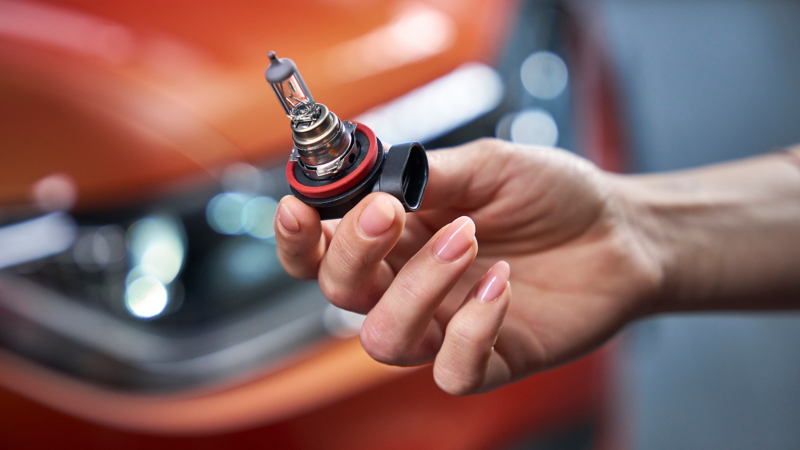 Volkswagen Original Glühlampe in einer Hand, im Hintergrund ein VW T-Cross