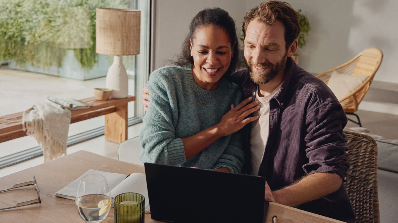 Frau und Mann sitzen am Tisch und schauen gemeinsam auf Notebook