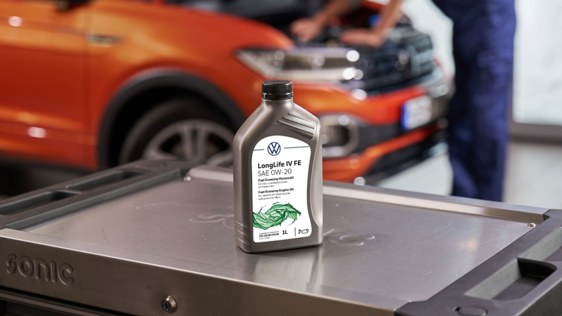 Bottle of Volkswagen Genuine LongLife IV FE Engine Oil on a roller container, a VW T-Cross in the background
