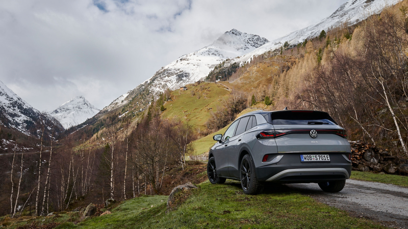Ein VW ID.4 parkt am Wegrand, im Hintergrund eine verschneite Berglandschaft