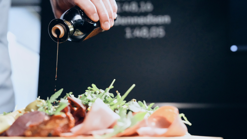 Jemand träufelt Balsamico auf einen Vorspeisenteller
