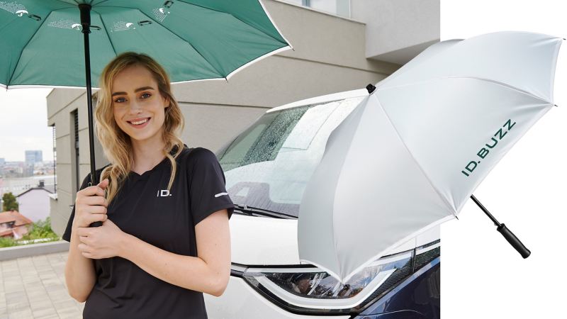 Eine Frau mit aufgespanntem ID. Buzz Regenschirm, im Hintergrund ein VW ID. Buzz – VW Zubehör