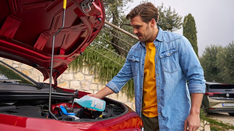 Man in front of open bonnet fills up VW screenwash concentrate