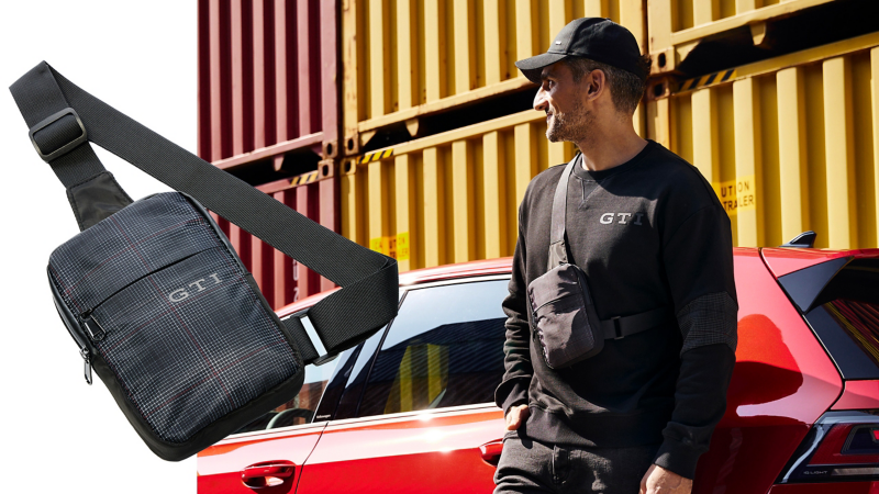 Man wears VW GTI shoulder bag and leans against red VW car