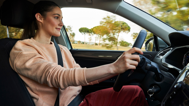 Strapped-in woman in the driver's seat of a VW with her hands on the steering wheel