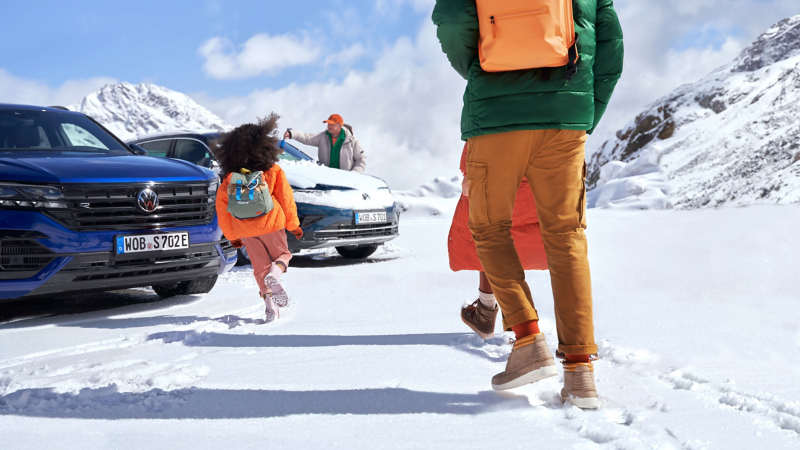 Familie geht zu einem vorgeheizten VW Auto in einer Schneelandschaft