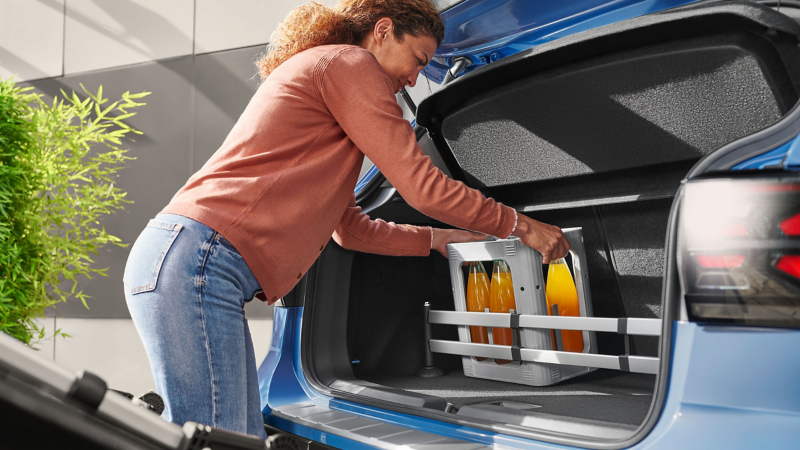 Woman loads luggage compartment, the luggage compartment plug-in module by VW Accessories fixates a beverage crate