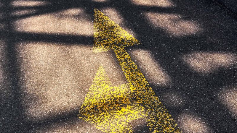 Eine gelbe Markierung auf der Straße zeigt einen Doppelpfeil, der nach links und geradeaus zeigt