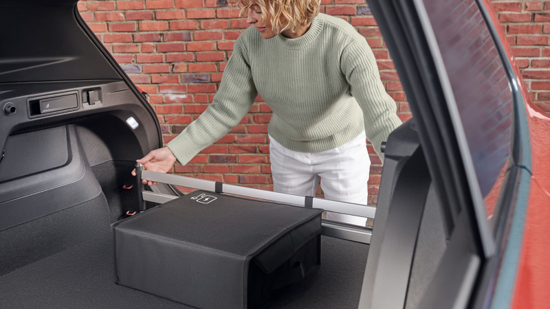 Kobieta montuje odpinaną ściankę do bagażnika z oferty Akcesoriów VW w bagażniku samochodu VW