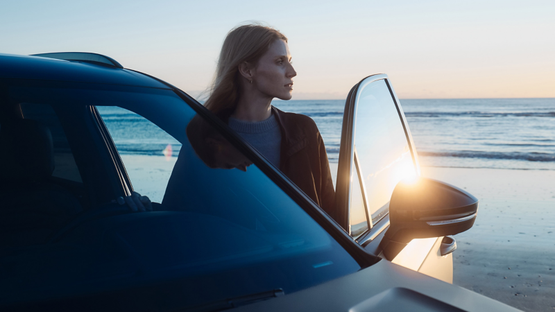 Frau steht an offener Fahrertür eines VW Touareg R FINAL EDITION und blickt in die Ferne, im Hintergrund das Meer