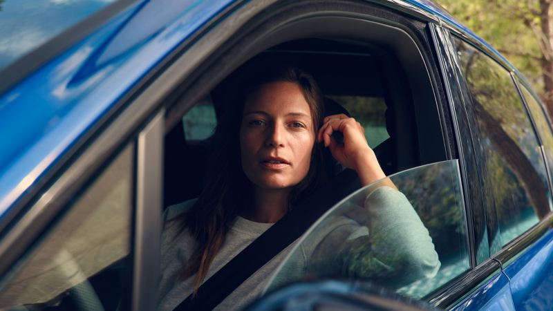 Una donna è seduta sul sedile del conducente e guarda attraverso il finestrino laterale aperto di un’auto Volkswagen