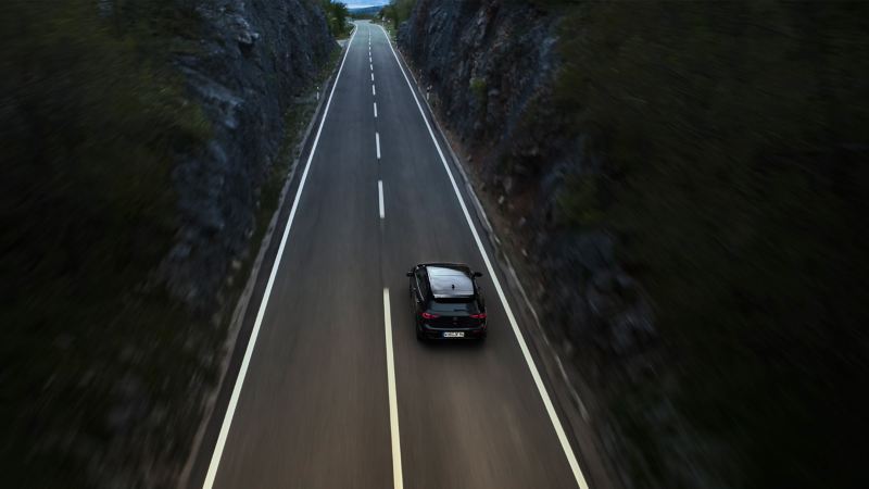 Vogelperspektive auf VW Golf R Black Edition, der auf Straße zwischen zwei Bergen fährt