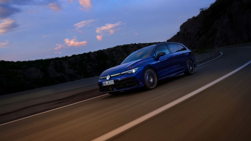 Une VW Golf R Variant, feux allumés, circule sur une route au crépuscule