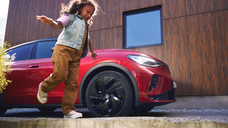 Mädchen läuft um VW ID.4 GTX, der vor modernem Haus parkt