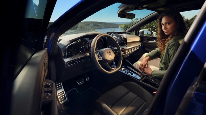 Une femme est assise sur le siège du passager avant d’une VW Golf R, avec vue sur le Digital Cockpit Pro et le système d’infodivertissement