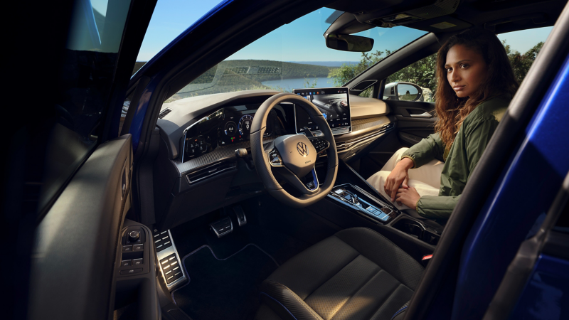 Une femme est assise sur le siège du passager avant d’une VW Golf R, avec vue sur le Digital Cockpit Pro et le système d’infodivertissement
