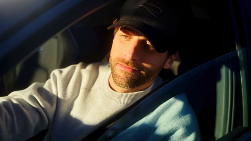 Un homme est assis sur le siège du conducteur, ceinture bouclée, et regarde par la vitre