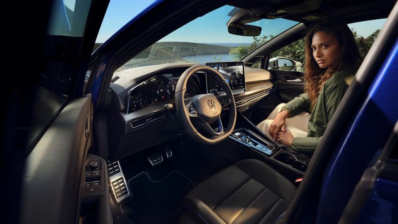 Frau auf Beifahrersitz eines VW Golf R, „Digital Cockpit Pro“ und Infotainment-System sind zu sehen