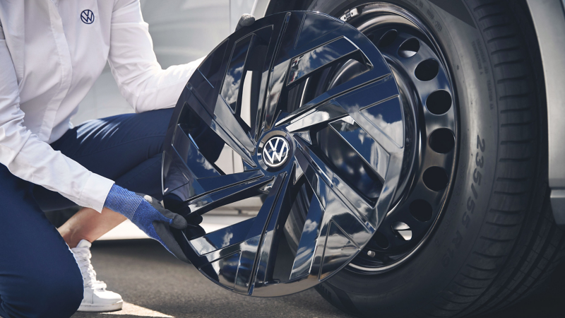 VW Servicemitarbeiter montiert schwarze VW Radkappe auf Stahlfelge