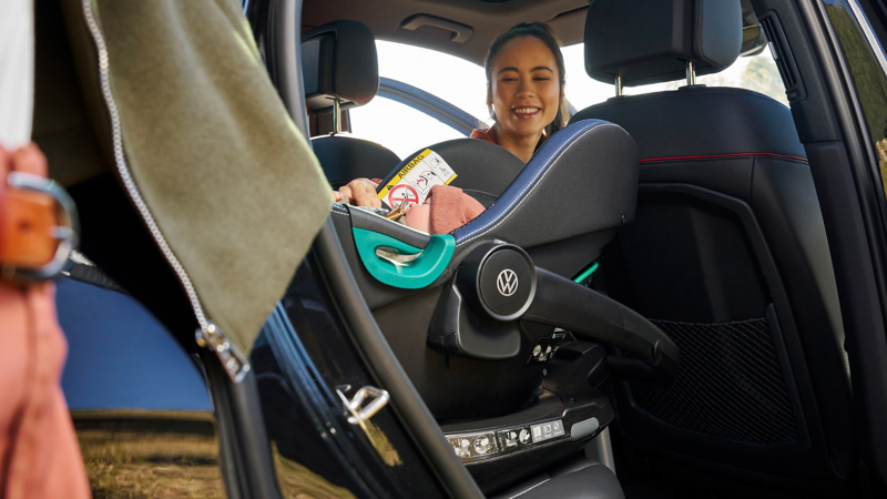 Frau schaut zu einem Baby, das im VW Zubehör Kindersitz „i-SIZE Babyschale“ liegt