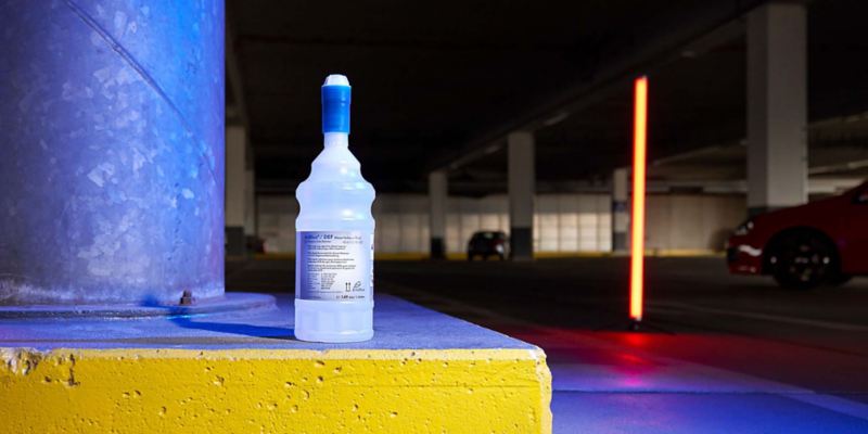 Vista di un flacone di liquido AdBlue adagiato sul pavimento di un'autofficina.