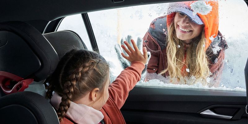 A mother looks through the frozen window into the warm interior of the car at her daughter – auxiliary heater from VW