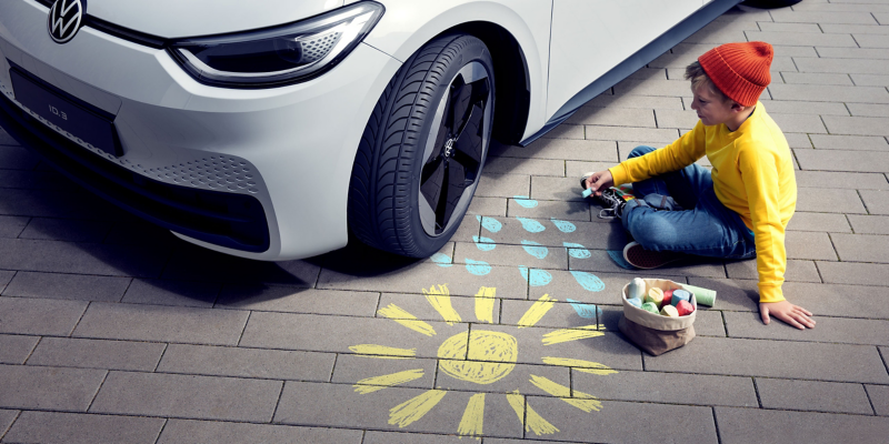 Un niño sentado frente a un VW ID.3 con llantas genuinas dibujando un sol con gotas de lluvia en la calle