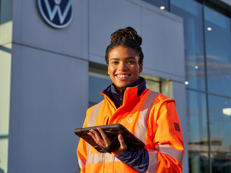 En kvinde i orange VW jakke står foran en forhandler med en ipad i hånden