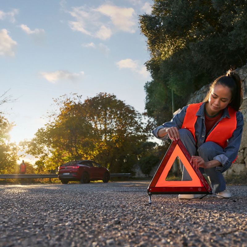 Woman with safety vest sets up warning triangle, in the background a VW ID.5 GTX