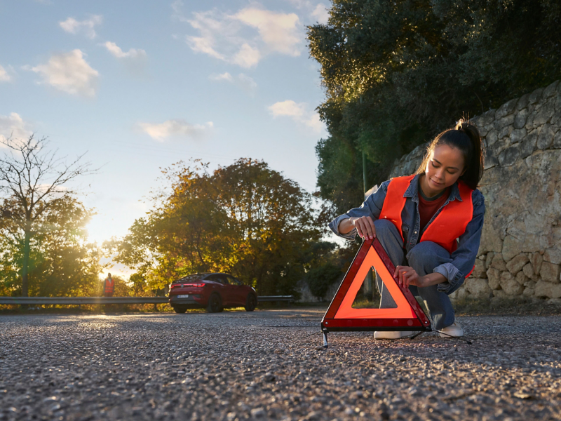 Woman with safety vest sets up warning triangle, in the background a VW ID.5 GTX