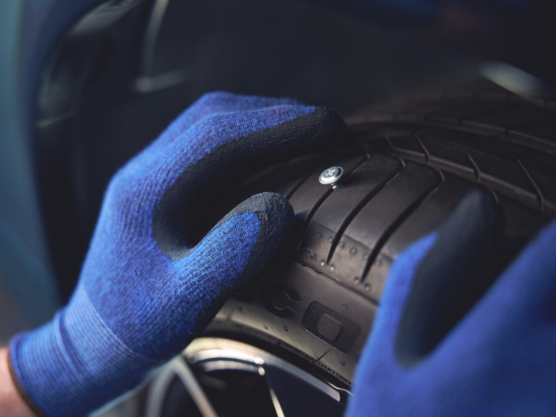 Jemand fässt mit blauen Handschuhen an VW Reifen, in dem ein Nagel steckt – VW AirStop® Reifen